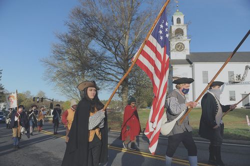 Jackie Kiernan carries the flag as the Sudbury Companies of Militia and Minute and the Sudbury Ancient Fyfe and Drum Companie march from Sudbury Town Hall to Concord